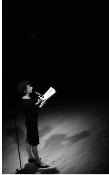Annie ZADEK en train de lire au micro, sur un fond noir.